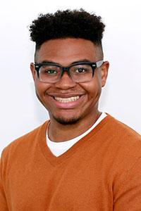 Man with brown skin wearing black glasses and orange sweater